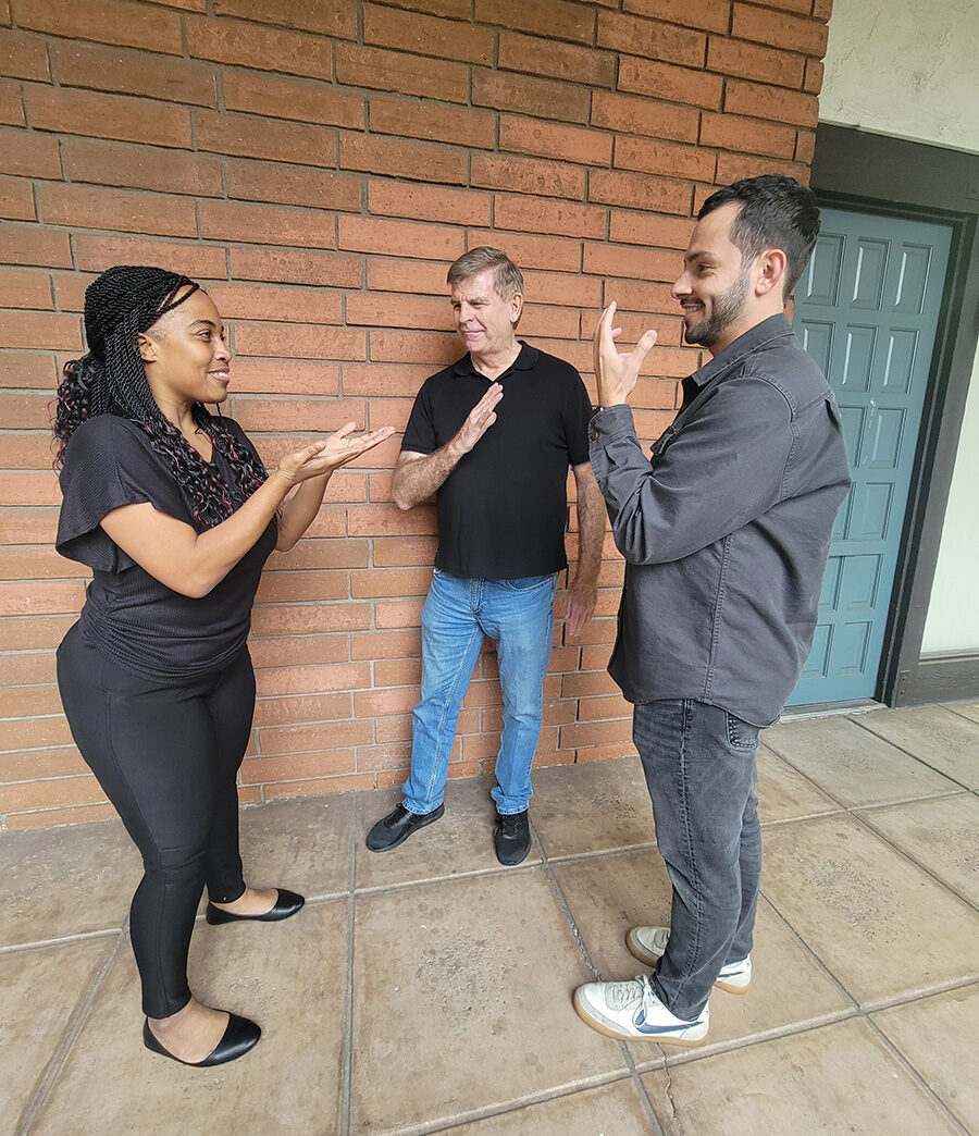 Deaf Services Team: Pamela, Jet and Tobias having conversation in ASL outside in front of brick wall