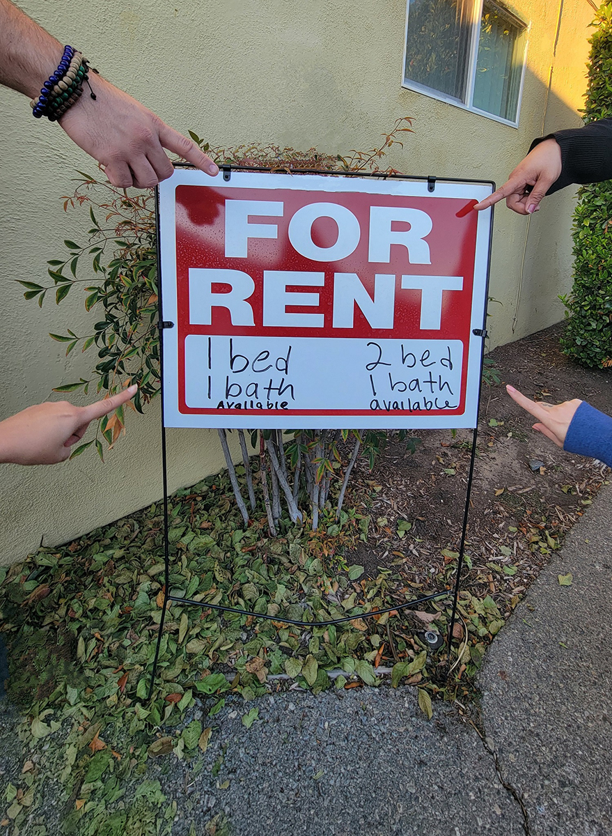 DMC Housing pointing to red and white apartment for rent sign outside.