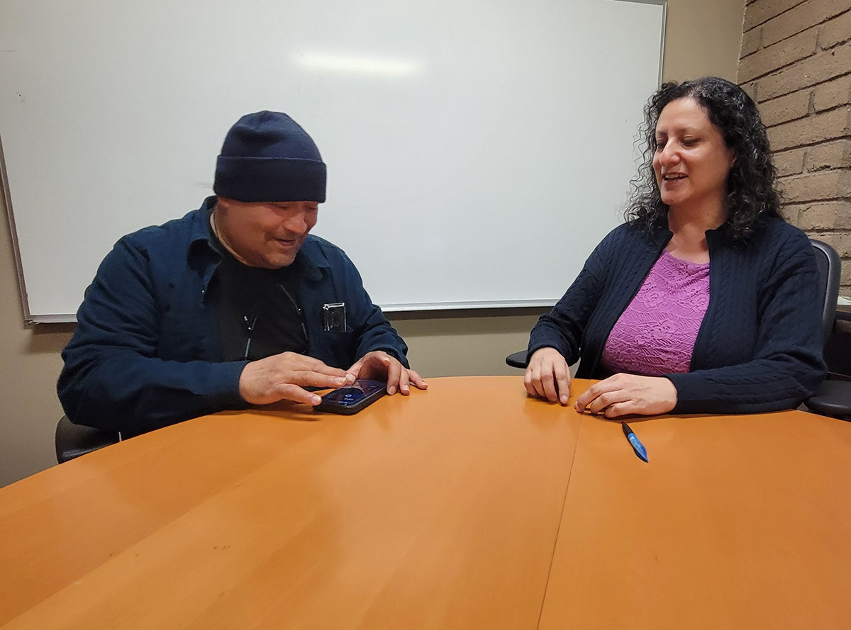 L-R: Consumer practicing using voiceover as Gabriela Alvarez, Independent Living Skills Instructor for the Blind guides consumer through process.