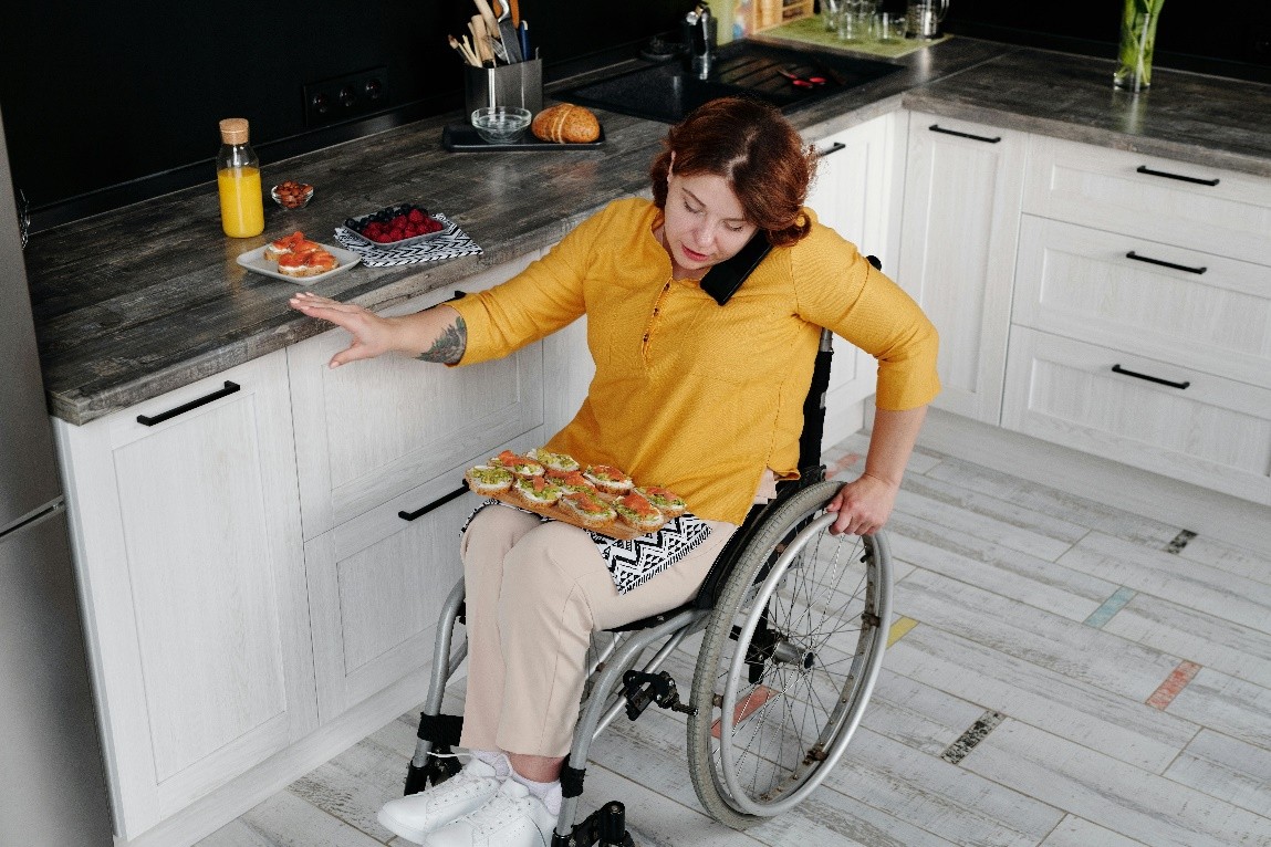 Person with disabilities in kitchen multitasking daily living skills preparing a meal in the kitchen while talking on the phone using communication social skills navigating use of a wheelchair at the same time safely. 