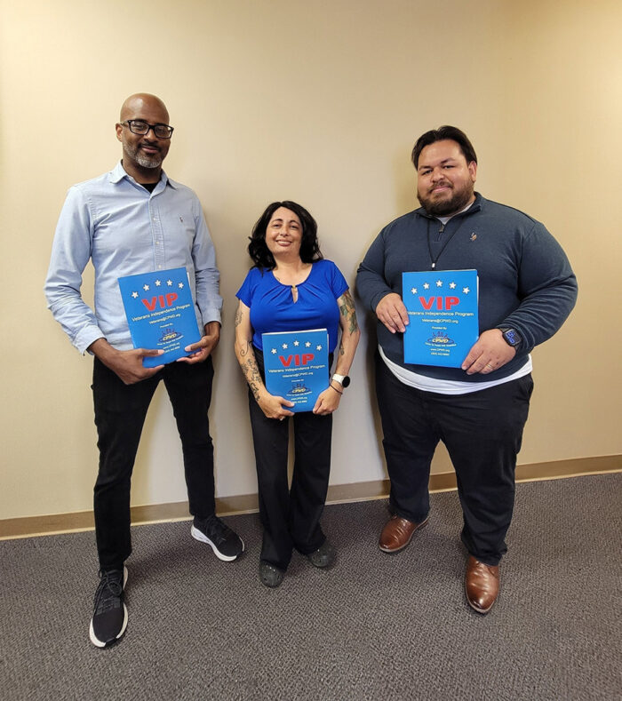 L-R: Andrew Toney, VIP Advisor Los Angeles, Marysol Cuadrado, Lead VIP Advisor and Luis Alvarez, VIP Advisor OC/LA standing together holding VIP information packet standing in front of tan wall inside DMC offices smiling.