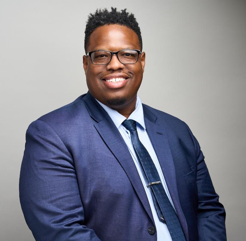 Head shot of Alvin who is wearing glasses and a blue suite and tie