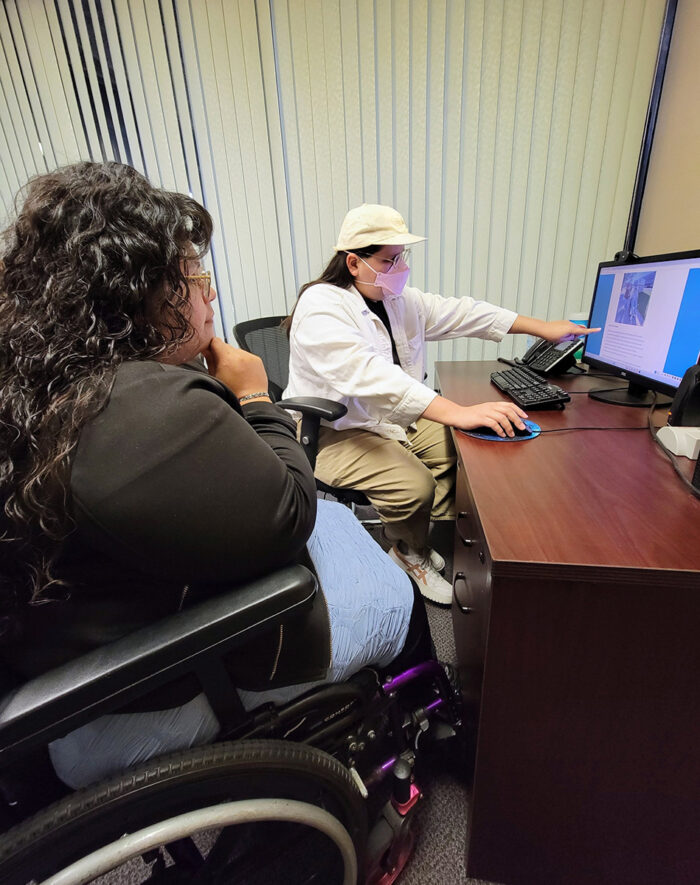  Luz and Nelly together at desk going over the DMC Youth Connect webpage on computer inside DMC for transitions which shares what happens in the DMC Youth program