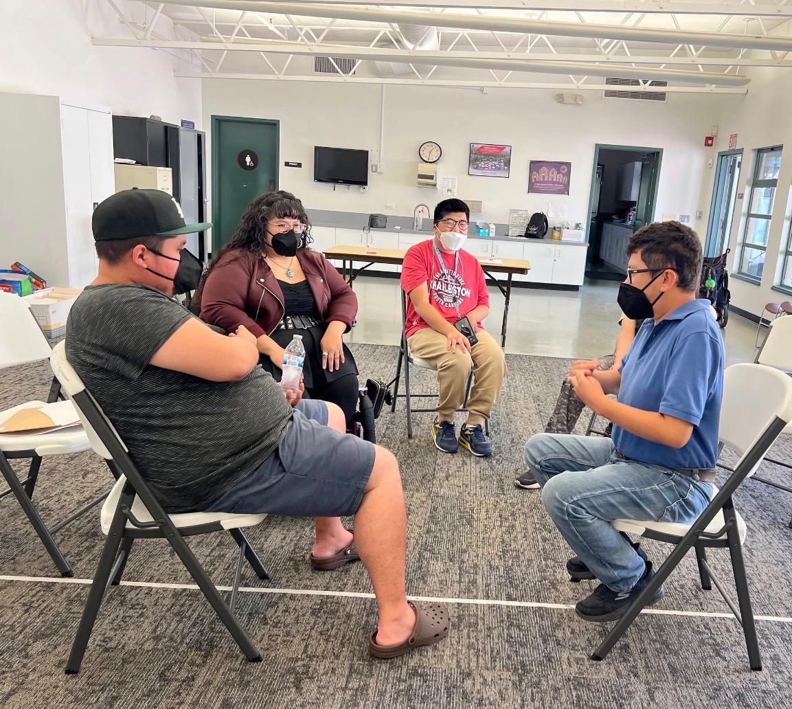  Nelly providing activity instructions to three cross-disability youth who are sitting in chairs.  