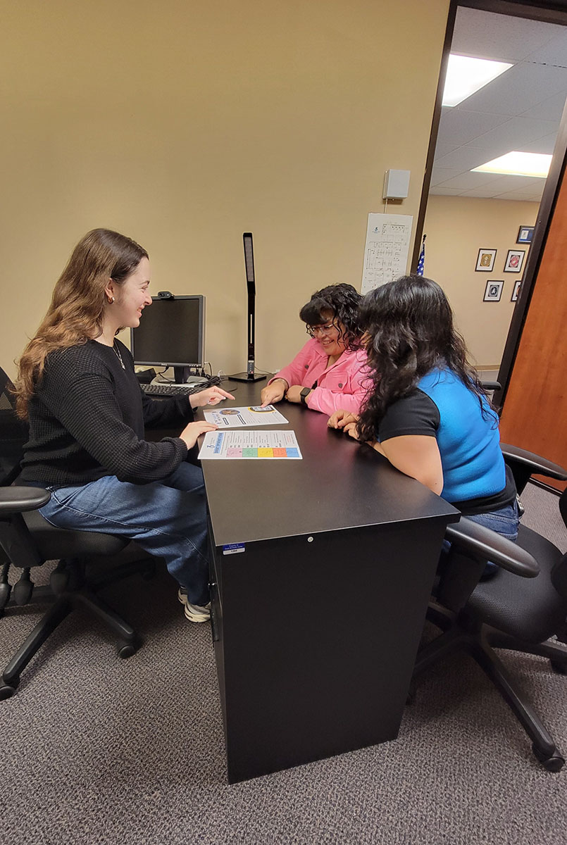 BreeAnna DMC Systems Change Advocate  sharing information about intake with nelly and Mareli in office at desk