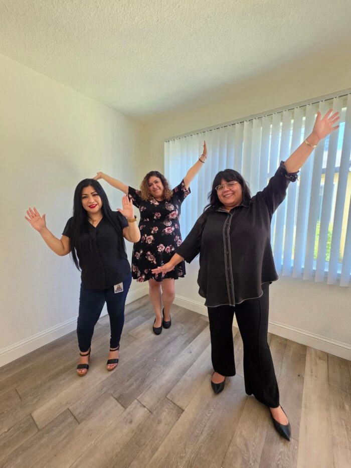 Housing Team L-R: Monica, Mari and Paola celebrating consumer with Welcome Home hands of celebration in the air smiling inside new apartment