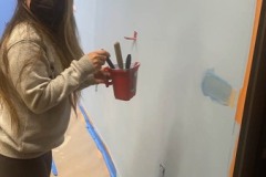 Photo-4-Pictured-DMCs-Ruth-is-ready-to-paint-a-wall.-Holding-a-painters-cup-brushes-are-being-selected-for-the-job