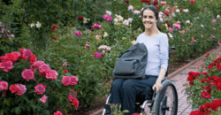 Picture-of-woman-in-wheelchair-with-tote-on-her-lap-rolling-on-pavers-through-a-rose-garden.