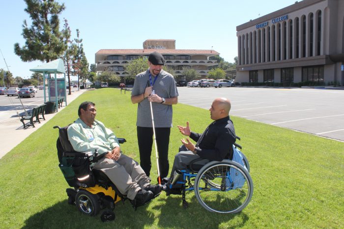 Peer support 3 men with disabilities talking on grass