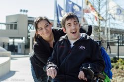 Young adult in power chair with attendent with nursing home in background .