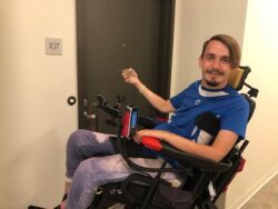Man in wheelchair using key to open door.