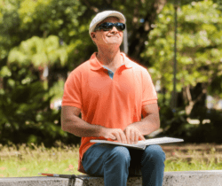 Man in orange shirt reading braille book.