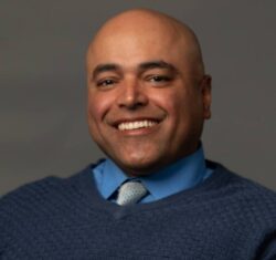 Smiling man in blue sweater and tie.