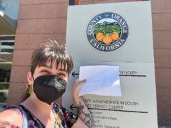 Person in a face mask by Orange County sign.