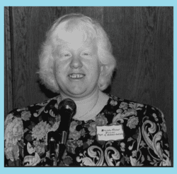 Pictured standing in front of a microphone, Brenda Premo is speaking in the community advocating for disability rights with Department of Rehabilitation