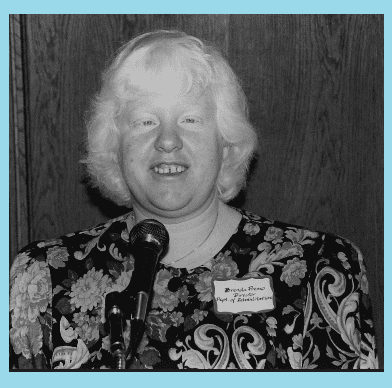 Pictured standing in front of a microphone, Brenda Premo is speaking in the community advocating for disability rights with Department of Rehabilitation