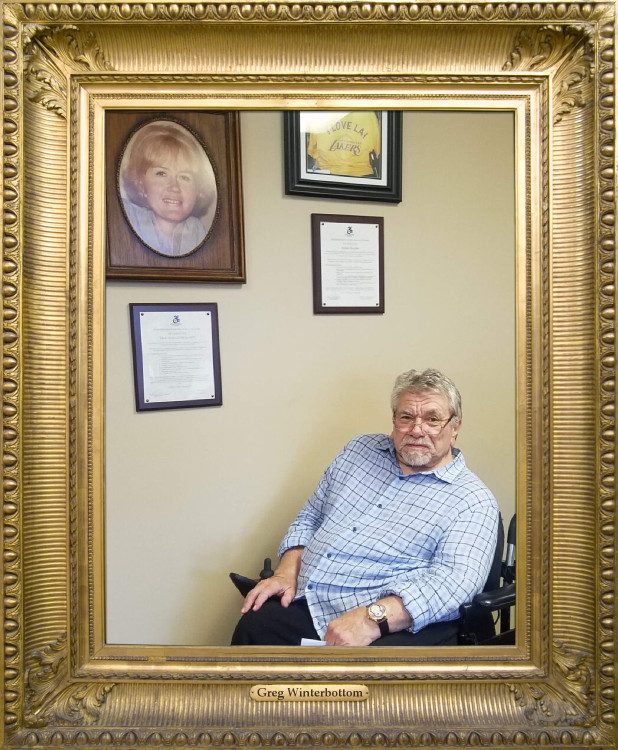 Pictured, Greg Winterbottom, DMC’s Original Board President/Chair visiting DMC; wearing a blue checkered shirt, sitting in his wheelchair underneath a photo of our Founder, Dayle McIntosh