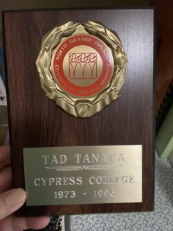 This is a photograph Tad’s family took of a plaque he received for his service from Cypress College. It is a wooden plaque with a gold leaf crest with red center reading “North Orange County Community College District“. The inscription on the gold plate of the plaque says Tad Tanaka, Cypress College 1973-1996.