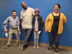 Four people smiling in front of a blue wall.