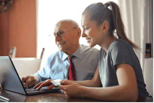 Pictured Older Adult with younger person being assisted with use of a computer