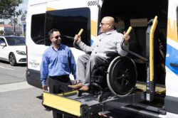 Person smiling on OCTA Access Wheelchair Lift being assisted by driver