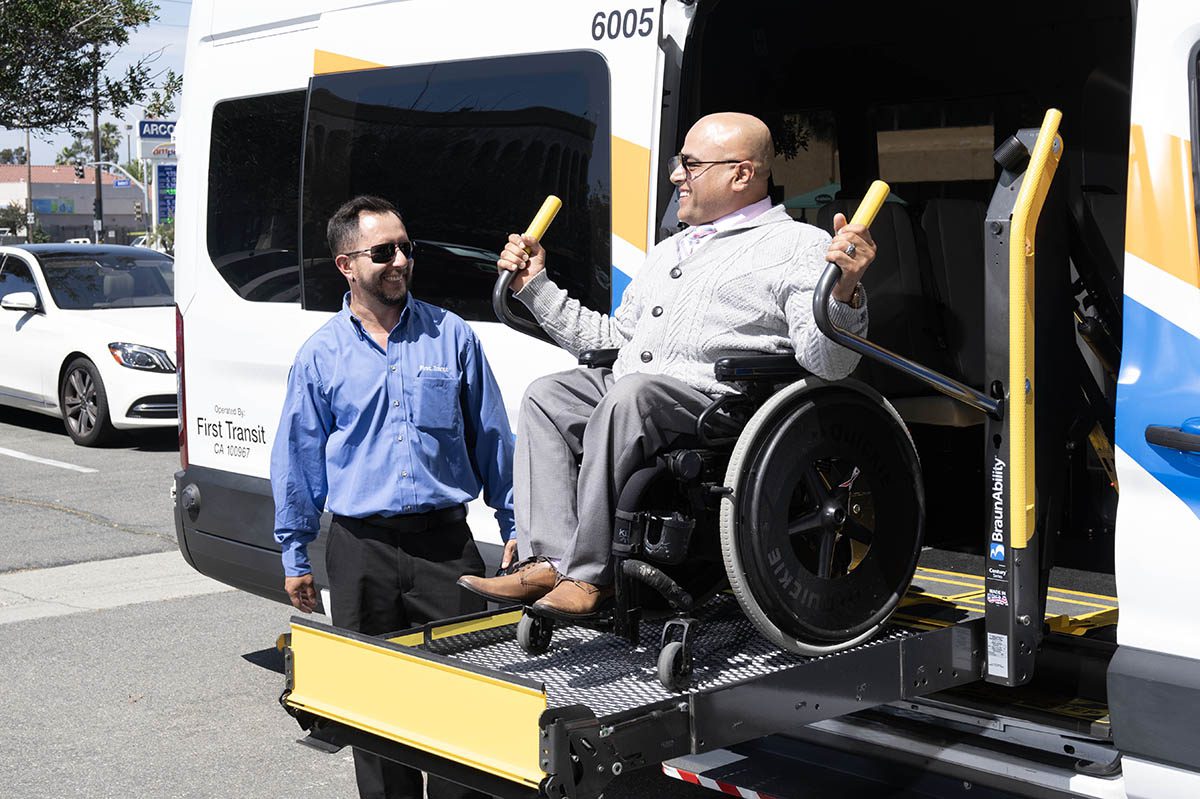 Person smiling on OCTA Access Wheelchair Lift being assisted by  driver