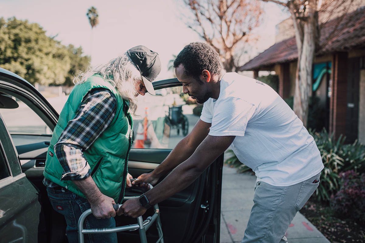 Individuals Relocating. Pictured Older adult receiving help from vehicle into Skilled Nursing Facility