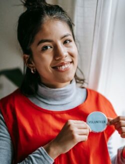 Pictured: person standing smiling showing off volunteer button feeling the reward of meaningful work.