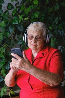 Elderly woman using phone with headphones.