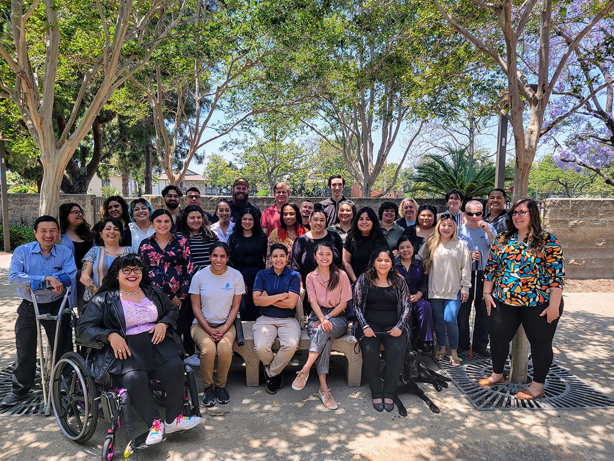 Team DMC Group Photo 2024 gathered with Board member Katy, smiling and posing with trees in the background