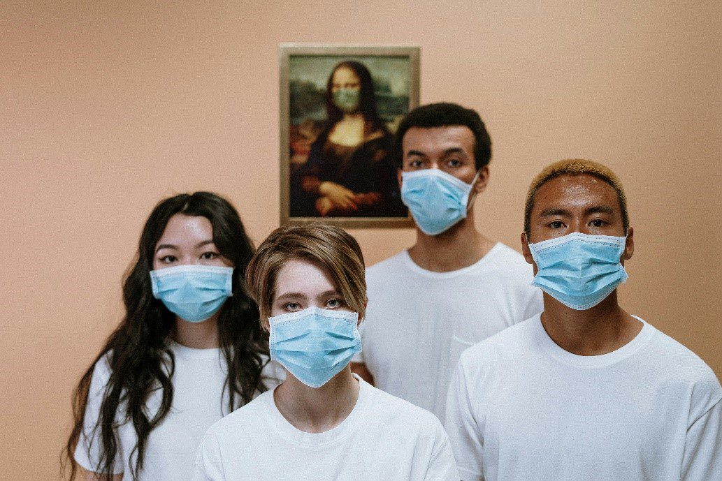 Four individuals wearing face masks and white T-shirts standing in front of a masked Mona Lisa painting.