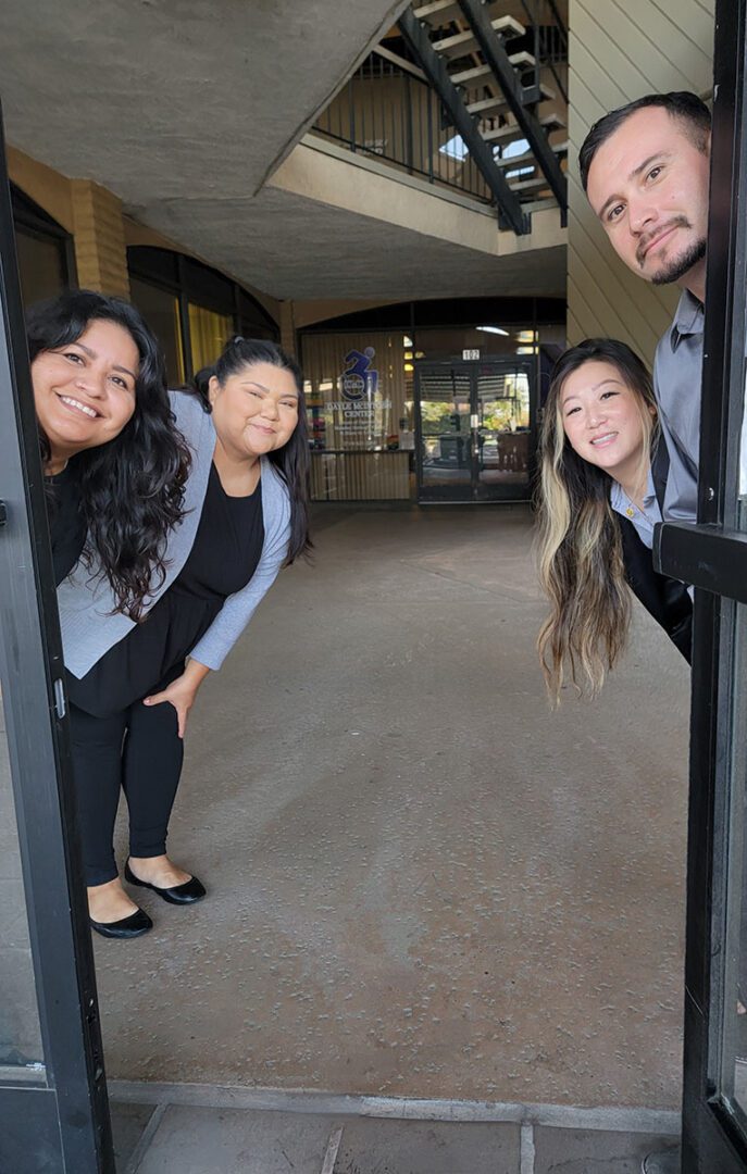 Pictured, DMC’s ADRC Team smiling while peeking heads around an open doorway with doors behind them. 