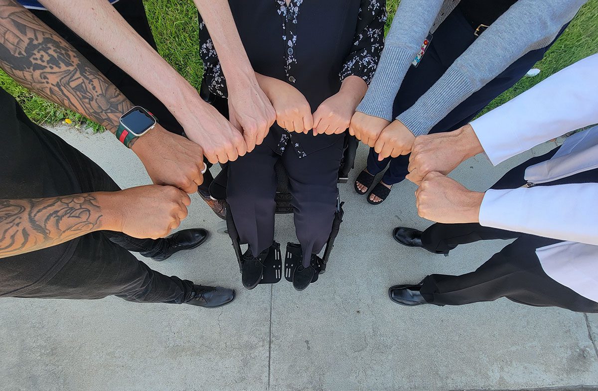 Pictured five sets of human BIPOC hands making fists in a half-circle looking like the shape of a sunrise. 