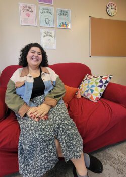 Ana sitting smiling on a red sofa with a colorful mosaic pillow next to her.