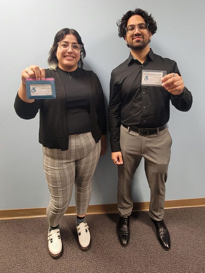 Pictured DMC Community Transitions Team Members Christabel and Babar standing showing their DMC badges. 