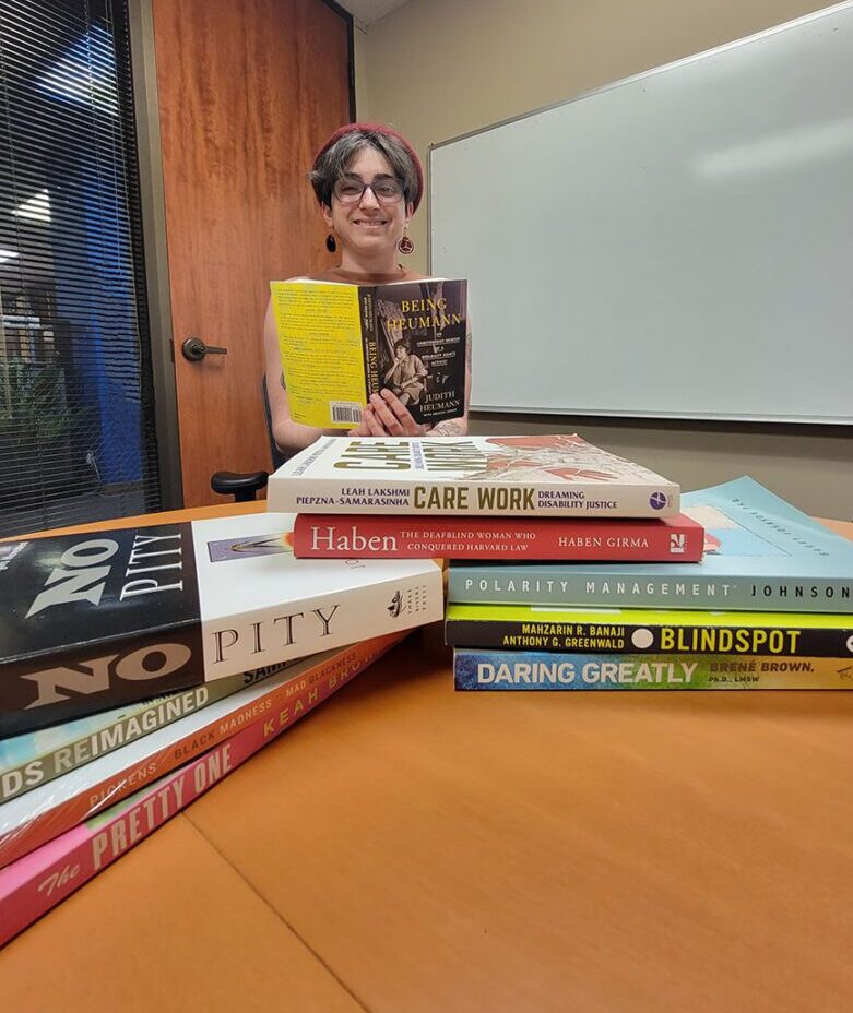 Beck writing in a notebook while smiling. In front of them are various books on different topics.