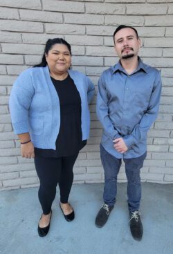 Pictured, DMC Community Living Advocates Esmeralda and Fernando standing smiling as they are happy to provide support for consumers to gain the home access accommodations they need.
