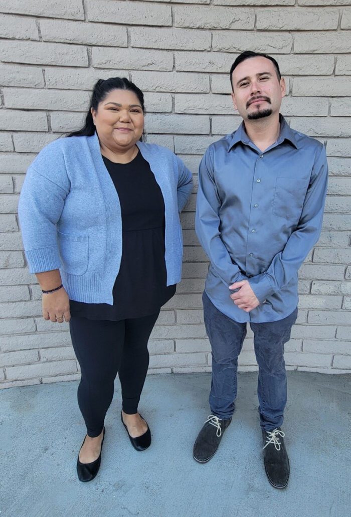 Pictured, DMC Community Living Advocates Esmeralda and Fernando standing smiling as they are happy to provide support for consumers to gain the home access accommodations they need. 