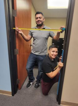 Pictured Home Access Team Ivan with measuring tape and Ana marking measurements with pencil on fame, as both are ensuring that measuring door dimensions are noted accurately to create access.