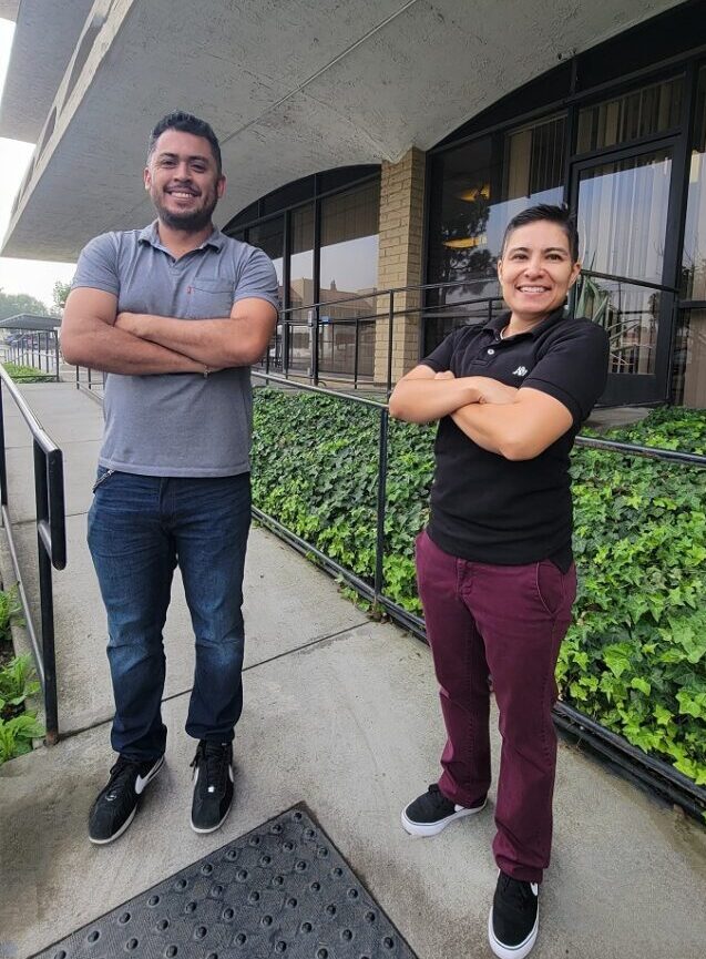 Pictured Ivan, Lead Home Access Specialist and Ana, Medi-Cal Home Access Specialist standing on access ramp outside of DMC smiling with fierce determination and support to advocate for individuals in need of Home Access modifications. 