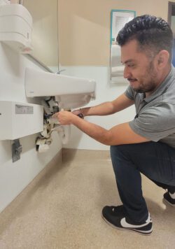 Pictured, Ivan using a screwdriver in bathroom to adjust PVC under sink