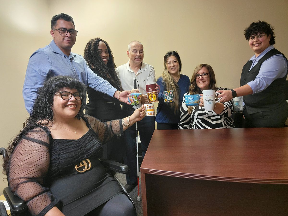 Pictured the Leadership Team around a desk, all holding coffee cups which vary in color and design. Left-to-Right – Nelly Gomez, Ivan Cortez, Pamela Torres, Paul Brennan, Ruth Cho, Brittany Zazueta, and Michelle Ramos.