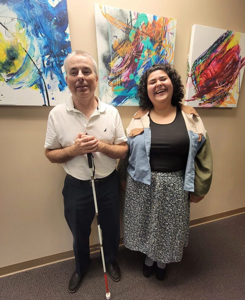 Pictured Paul and Anita Standing in front of a psychedelic colorful art wall. They are beaming with pride being able as a consumer’s success story is also a DMC Success Story.