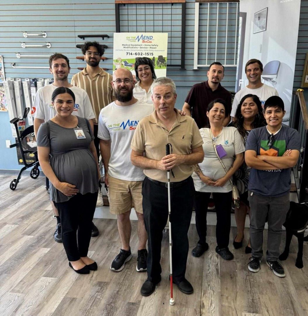 Pictured Team DMC Staff standing in group photo smiling with On the Mend Team at live event. Background features grab bar and home modification accessibility options mounted on wall.