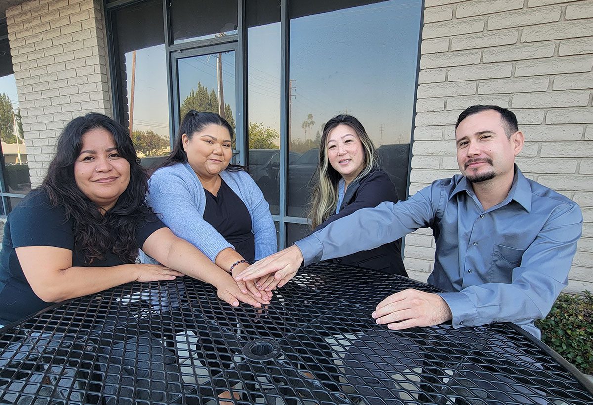 Pictured ADRC Team Mareli, Esme, Ruth and Fernando at a table with their hands joining forces in the center together, united and all-in to help older adults.