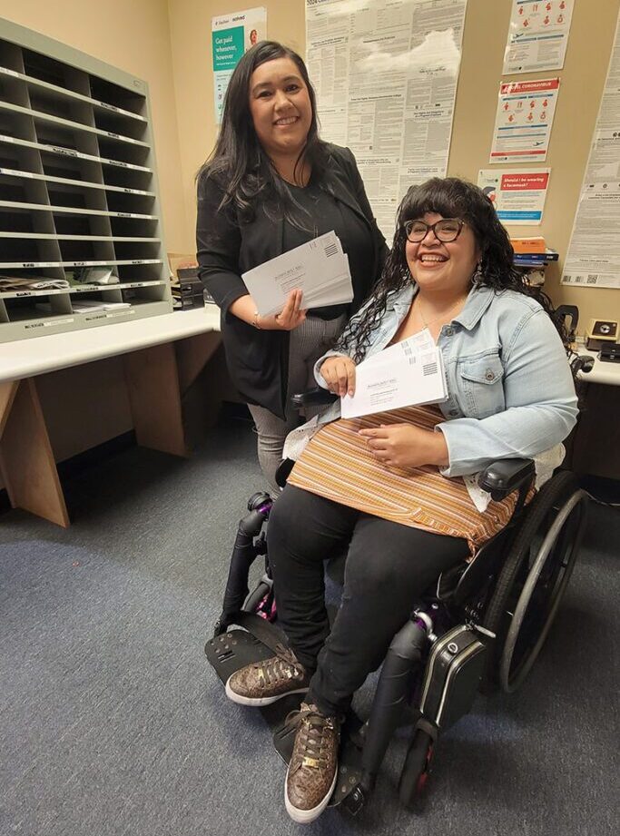 Bianca and Nelly smiling while working through DMC’s busy mailroom. Pictured, both of them holding incoming envelopes to DMC!