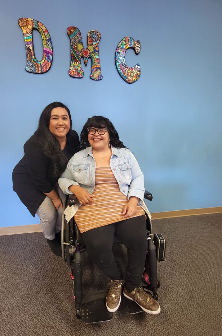 Pictured Bianca and Nelly smiling proudly in front of DMC’s blue wall with rainbow psychedelic mosaic artwork lettering for the initials D-M-C