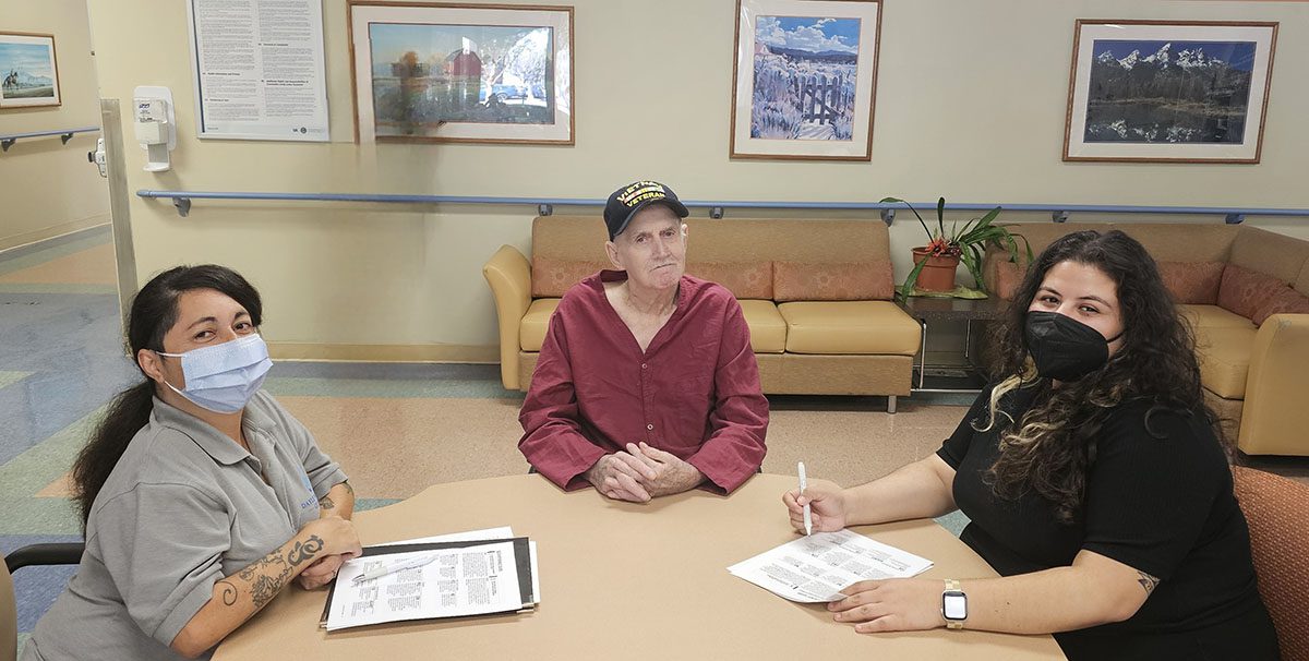 Pictured, Team DMC’s Marysol and Wendy sitting at a table with paperwork working to advocate for a Veteran at the Long Beach VA.