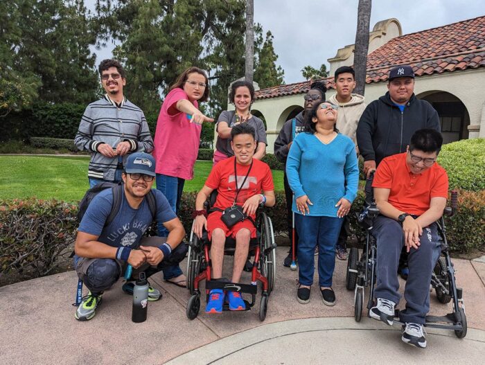 Youth participants gathered together outside of DMC as part of the DMC Youth Connect program. Behind them are trees, grass and bushes surrounding the building. 