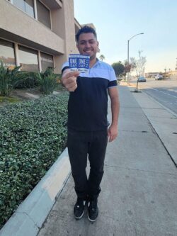Ivan smiling and holding two OC Bus Day Passes for people with disabilities.